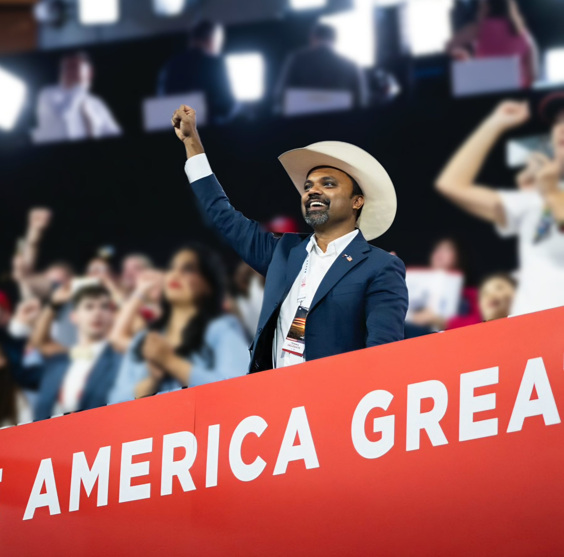 Abraham George raising a fist at a rally in front of a Make America Great banner
